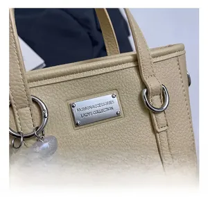 Detail view of beige pebbled leather bucket bag with silver logo plate and pearl charm