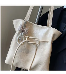 Dettaglio della borsa tote beige in pelle cerata con coulisse e ciondolo cuore e perle