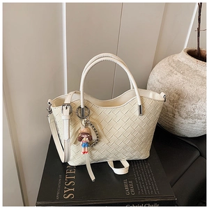 Detail of cream woven handbag with wavy edges and cute cartoon doll charm accessory