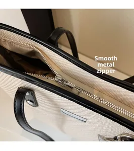 Detail of smooth silver metal zipper with black leather trim on a woven tote bag