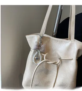 Détail d'un pendentif chic avec nœud et perles sur un sac cabas en cuir beige