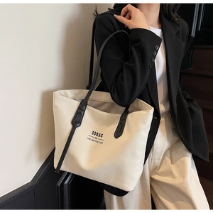 Minimalist cream canvas tote bag with black shoulder strap and text detail on model