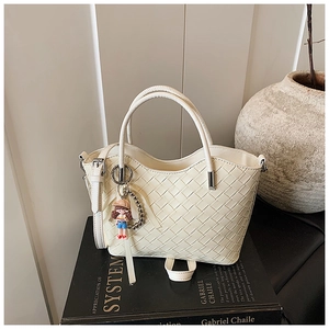Detail of cream woven leather bucket bag with top handle and cute girl doll charm
