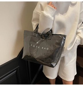Dettaglio di una grande borsa tote nera lucida con scritta TOTE BAG bianca indossata a spalla