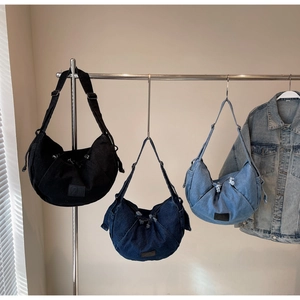 Crescent denim crossbody bags in black, dark blue, and light blue on a metal display rod