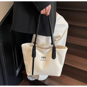 Minimalist beige canvas tote bag with black leather handles held by model on stairs