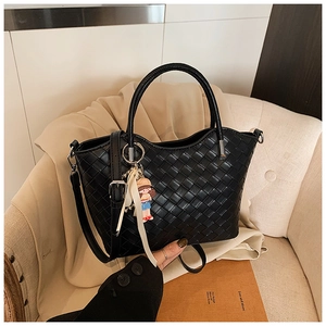 Close-up of black woven leather tote bag with girl pendant on a cream sofa