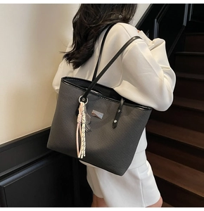 Detail of black woven tote bag with silver plate and tassel charm on model shoulder