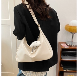 Detail of a cream-colored hobo tote bag with a cute plush cloud charm and wide shoulder strap