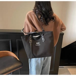 Close-up of a large black canvas tote bag being carried on the shoulder by a model
