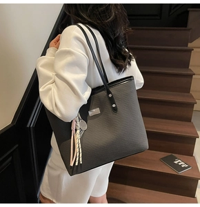 Detail of dark grey woven tote bag with silver metal tag and pink tassel charm