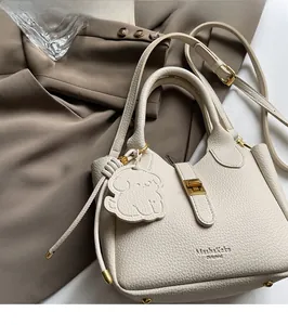 Detail of off-white lychee grain leather bucket bag with dog charm and gold hardware