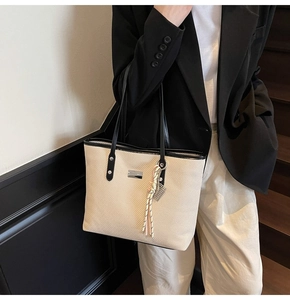 Detail of cream woven tote bag with black trim and colorful cord pendant on model