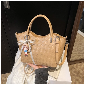 Detail of beige woven tote bag showing leather texture and decorative cartoon charm