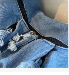Detail of blue denim fabric showing smooth black zipper closure and frayed fringe texture