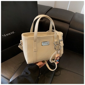 Detail of cream leather bucket bag with litchi texture and elegant pearl charm