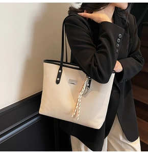 Detail of beige woven tote bag with slim black handles and silver metallic logo accent