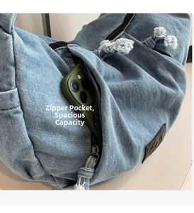 Detailed close-up of the zipper pocket on a washed denim crossbody bag with phone inside
