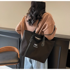 Detail view of large black canvas tote bag showing the side profile and long shoulder straps