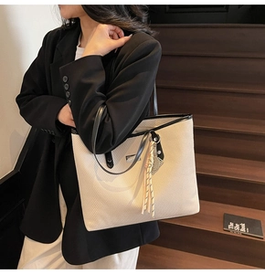 Detail of minimalist beige tote bag featuring black leather trim and tassel charm