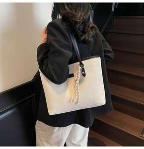 Detail of minimalist cream canvas tote bag with black leather straps and tassel decor