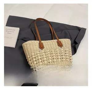 Macro view of woven straw tote bag featuring brown leather handles and hollow crochet detail