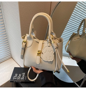 Detail of cream white pebbled leather handbag with gold twist lock and dog bag charm
