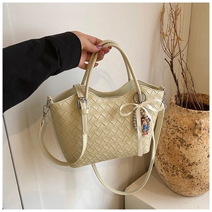 Detail of beige quilted tote bag with woven texture, bow ribbon and cartoon charm