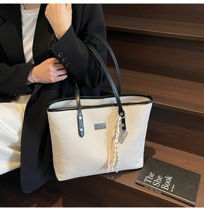 Detail of cream tote bag with black trim and tassel charm on wooden stairs