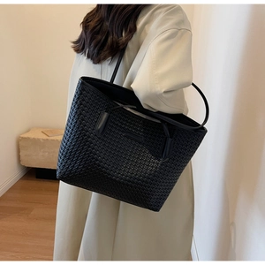 Detail of a large black woven tote bag showing texture and shoulder strap on model