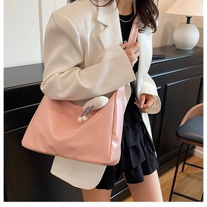 Pink crescent shoulder bag with plush charm shown in a stylish interior lifestyle setting