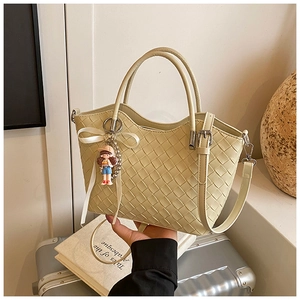 Detail of off-white quilted bucket bag with woven texture, bow, and doll charm