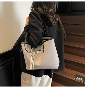 Detail of cream woven tote bag with black contrast trim and striped tassel on shoulder