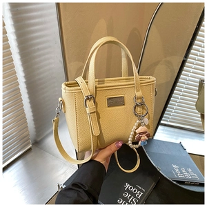 Detail of light yellow lychee pattern leather tote with pearl cartoon girl charm