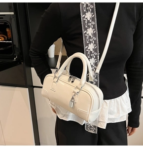 Detail of a creamy white patent leather Boston bag with silver lock and shoulder strap