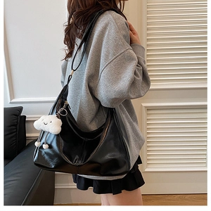 Detail of black leather tote bag with white plush charm worn on a shoulder