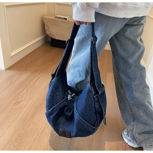 Detail of a navy denim crescent hobo bag with adjustable strap on a gray sweatshirt