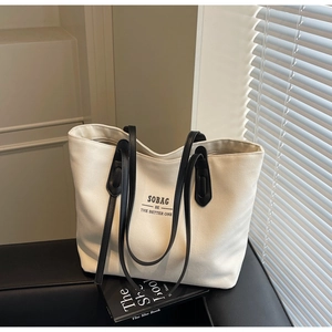 Detail of a cream canvas tote bag with black leather straps on a modern sofa
