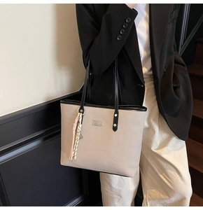 Detailed view of beige woven tote bag with black straps worn over a black blazer