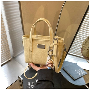 Detail of yellow bucket bag with lychee texture, pearl charm, and metal logo plate