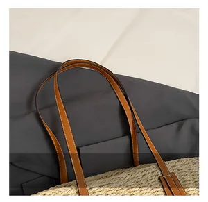 Detail of the brown leather handles with white stitching on a natural straw woven tote bag