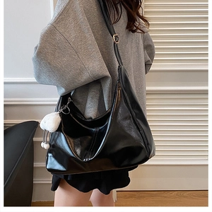 Detail of glossy black tote bag with gold buckle and white plush cloud charm on shoulder