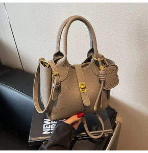 Detail of taupe lychee leather bucket bag with golden twist lock and bear charm accessory