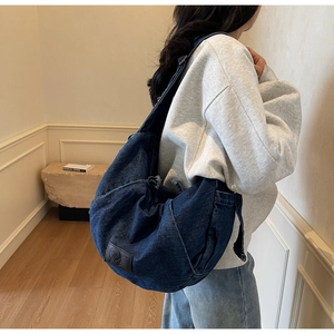 Close-up of blue denim crossbody bag with black leather logo patch and frayed edge detail