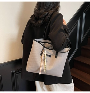 Detail of grey textured tote bag featuring pink tassels and black leather straps