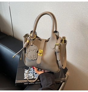 Detail of taupe lychee leather handbag featuring a gold buckle and dog-shaped charm
