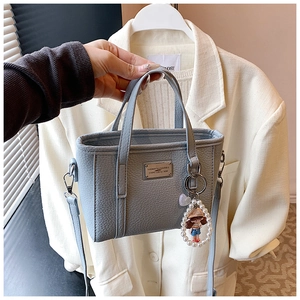 Detail of grey-blue litchi grain crossbody bag featuring a pearl doll charm
