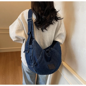 Detail of blue denim crescent bag featuring brown leather logo patch and adjustable strap