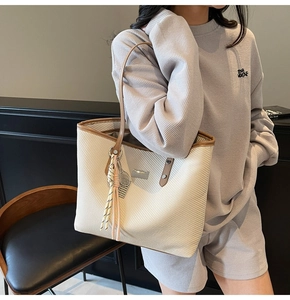 Detail of creamy woven tote bag with brown leather trim and tassel on a model shoulder