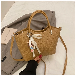 Detail of light brown woven tote bag featuring a white bow and cute cartoon pendant
